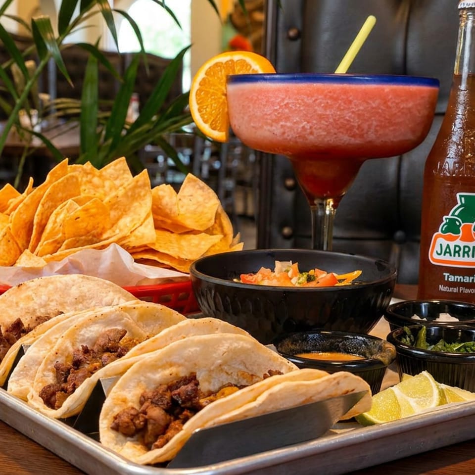 Tray of beef tacos, basket of tortilla chips, salsa, frozen margarita, and two Jarritos sodas.