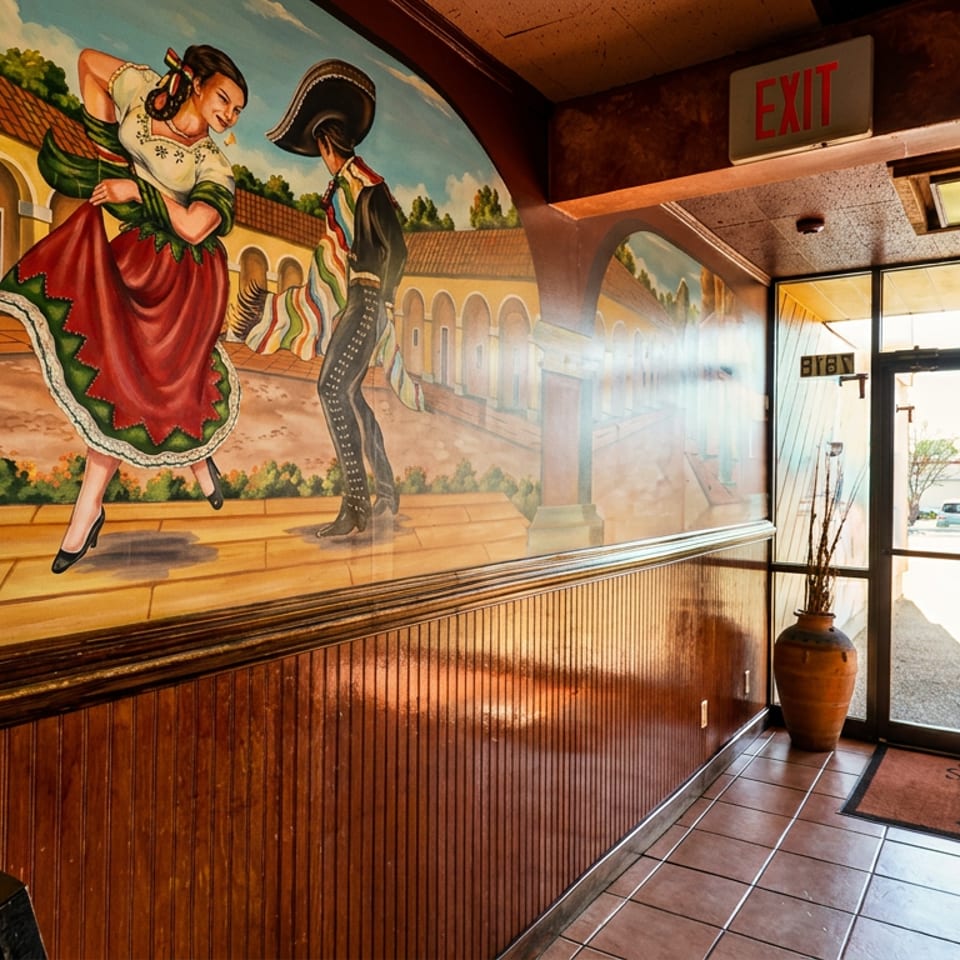 Vibrant mural of dancing figures above wood paneling, next to a glass entrance door.