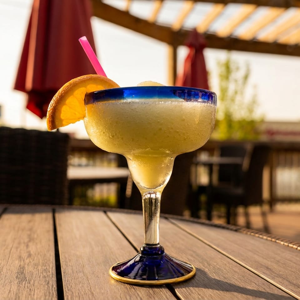 Frozen margarita with an orange slice and pink straw on a wooden patio table.