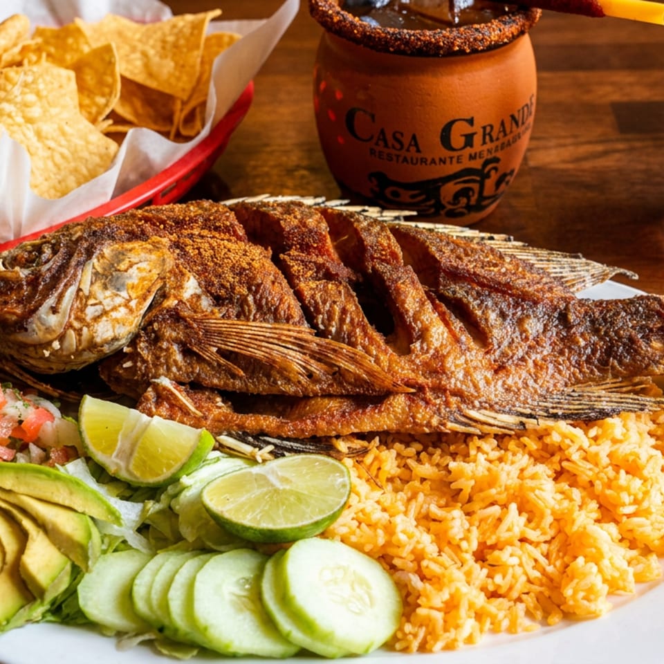 A whole fried fish with rice, salad, avocado, and two drinks, including a Casa Grande cup.