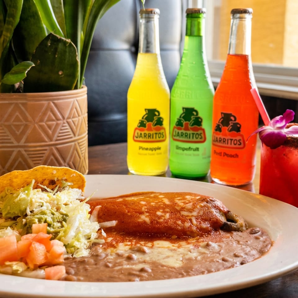 Mexican meal with a taco, enchilada, refried beans, three Jarritos, and a garnished red cocktail.