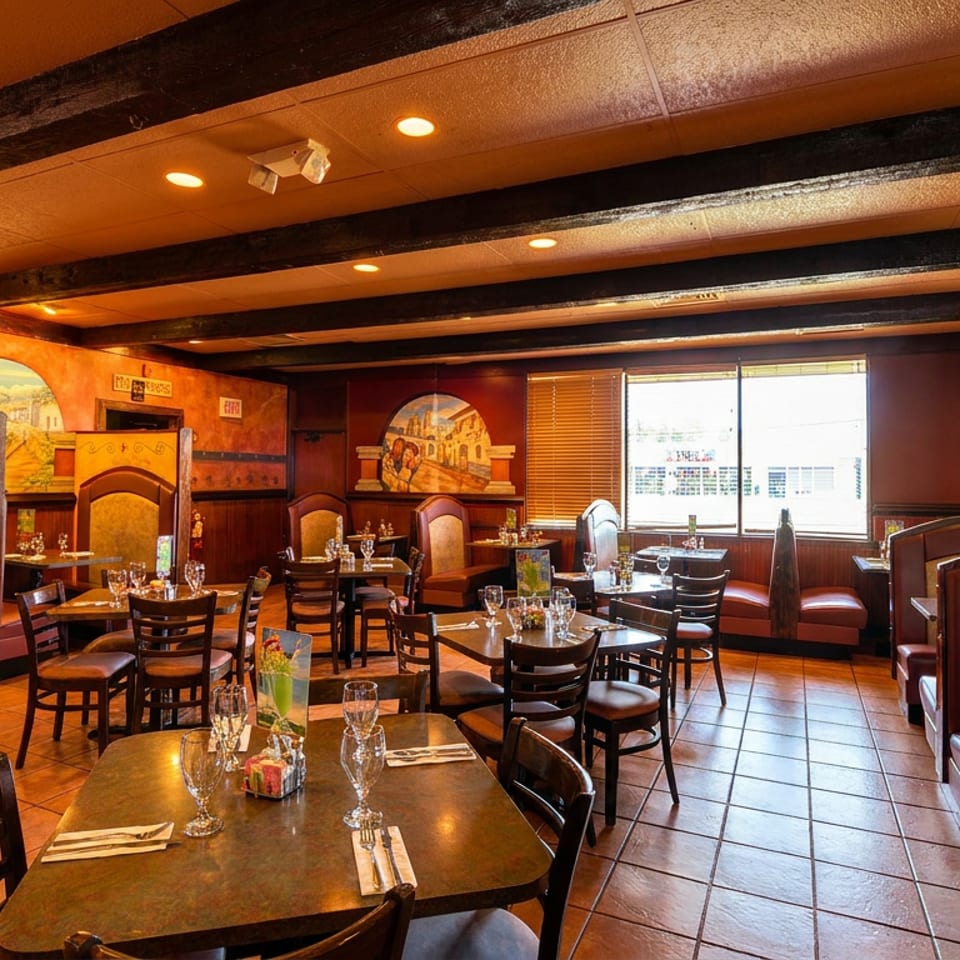 Warmly lit Mexican restaurant interior with tables, chairs, booths, and colorful murals on textured orange walls.